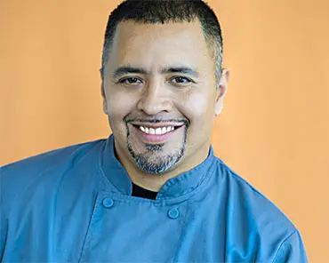 A man in blue shirt and black jacket smiling.